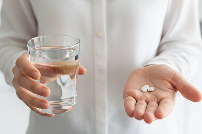 Рука держит таблетки и стакан воды